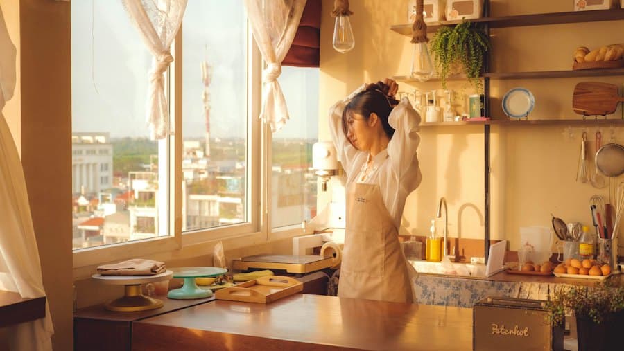 A woman tying her hair back in a sunny kitchen